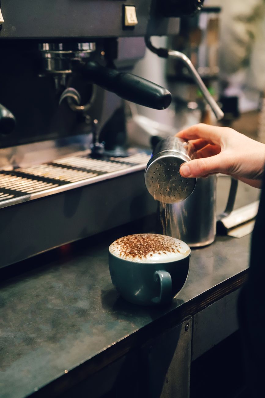 barista adding cocoa to fresh cappuccino